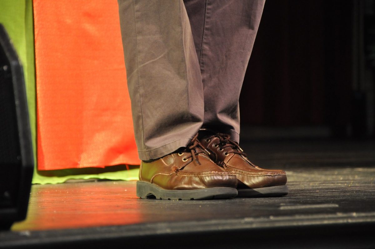 Man's legs on a stage. He is wearing loafers and casual brown dress pants.