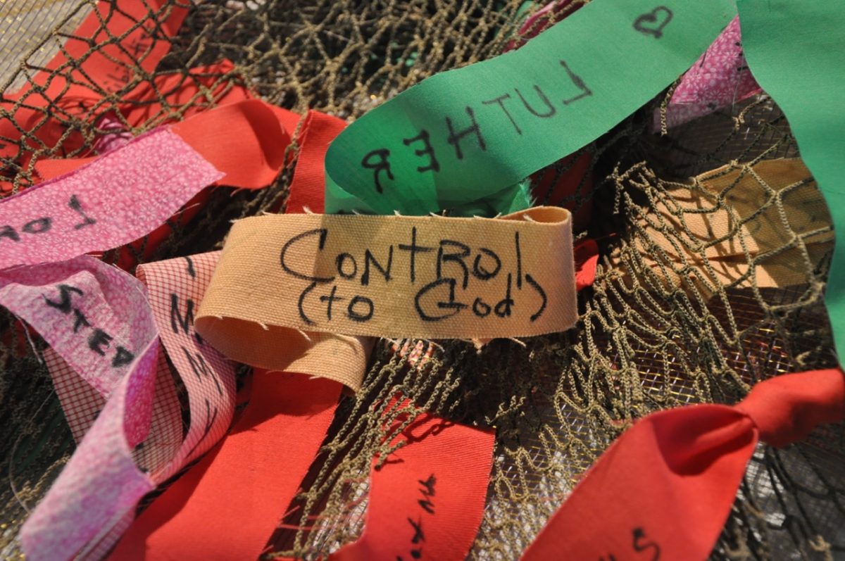 Strips of colored material with words and phrases written on them. Phrase in the center says "Control (to God)."